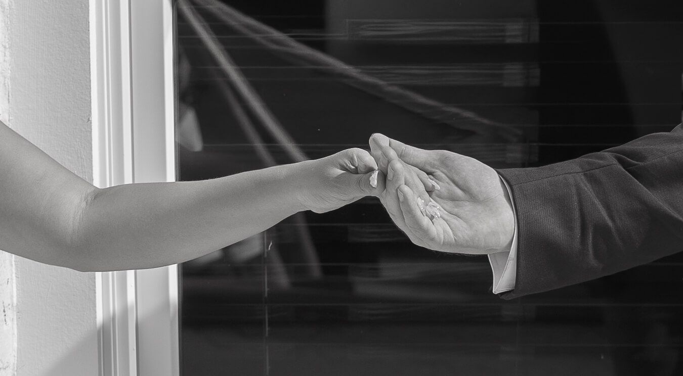 Black and white close-up of a bride and groom holding hands and exchanging small details during an intimate wedding moment.