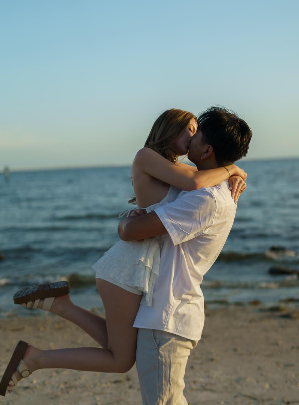 A man lifting his fiancée into the air for a passionate kiss on a Florida beach at sunset