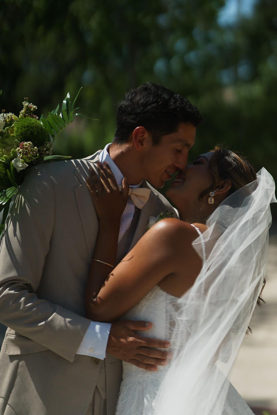 Romantic close-up of a bride and groom embracing outdoors, smiling with their faces close together in the sunlight