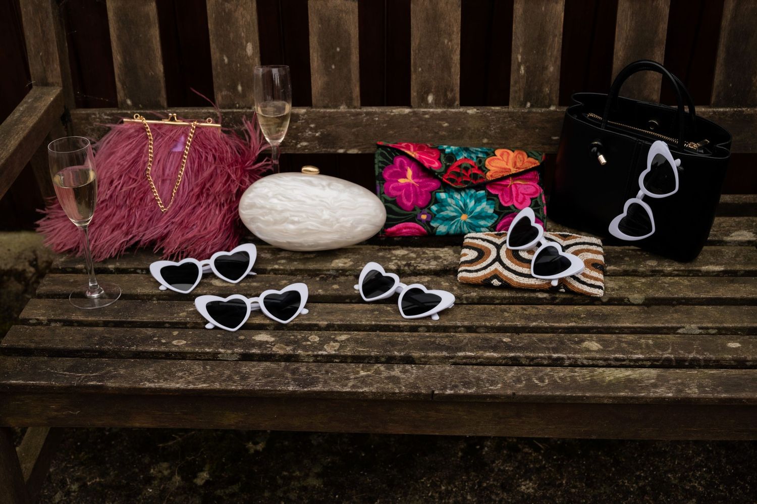 Handbags on a bench in various designs and colours, one is feathered, one has multicoloured sequinned flowers and another is a pearl design.