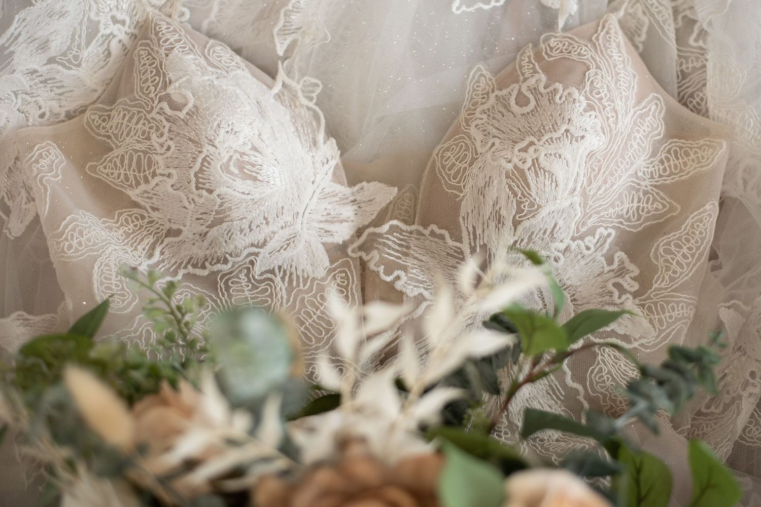 Pattered lace corset of a madilane wedding dress with a floral bouquet of green and brown foliage placed on top.