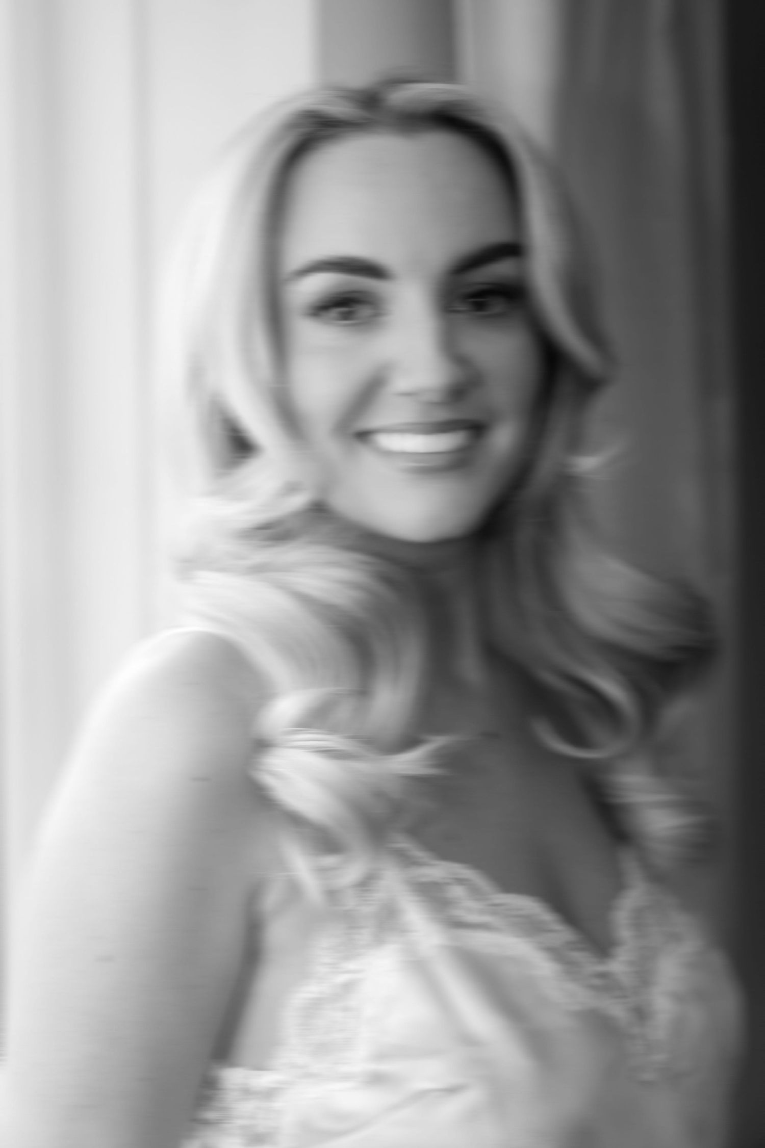Old fashioned blurry portrait of a smiling woman in a window with sweeping blonde curls wearing a lace camisole.