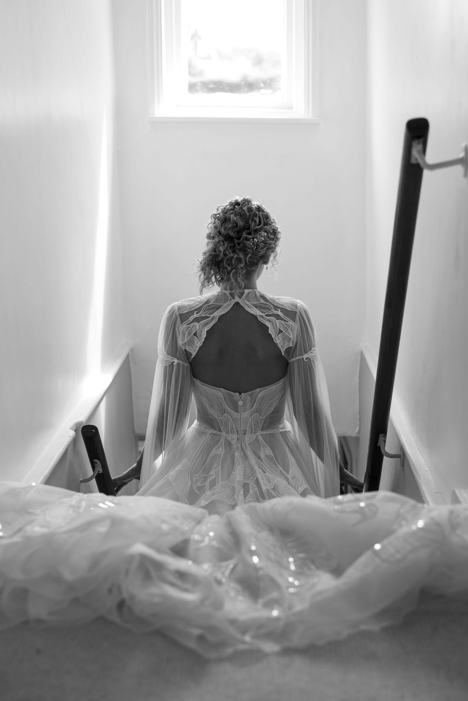 A bride descends a narrow staircase whilst the light from a small high window shining down on her and her long sparking dress.