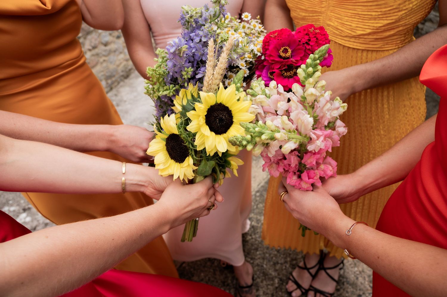 Sunflower, poppy and fox glove bouquets are held together in a bunch by a group of women wearing multicoloured dresses.