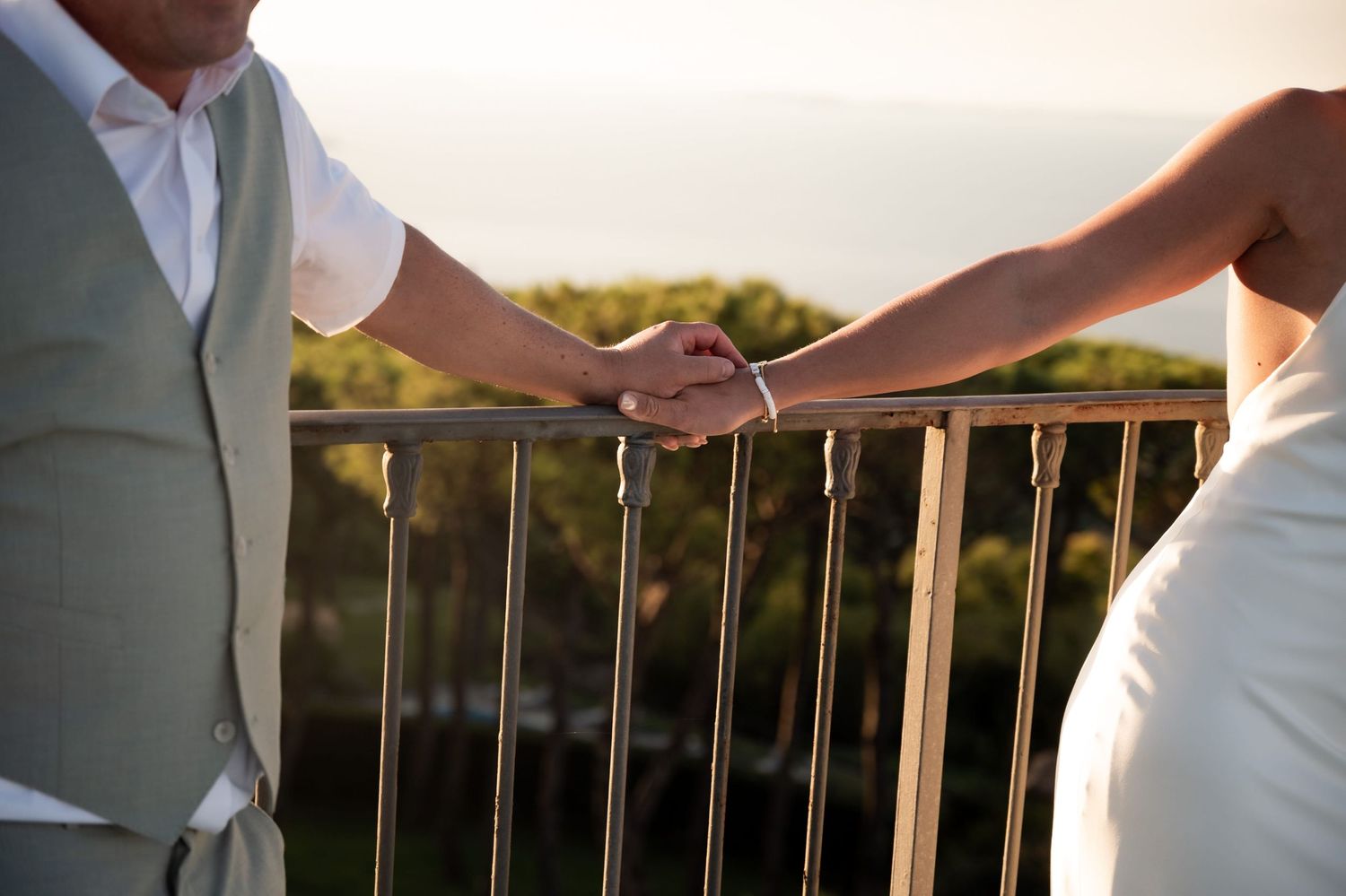 Woman holds on to a railing at sunset, her partner puts his hand gently on top of hers affectionately.