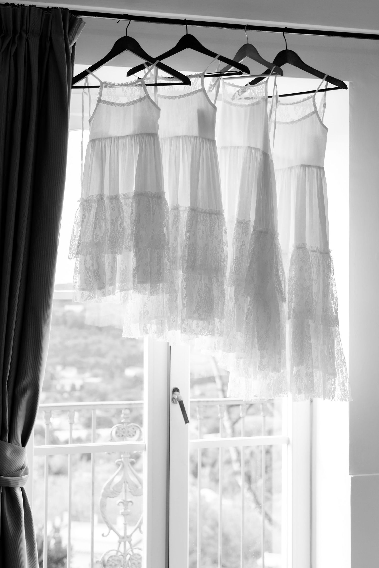 Four lace flower girl dresses hanging in a window, they are arranged in size order from a tiny dress at the front and go up in size.