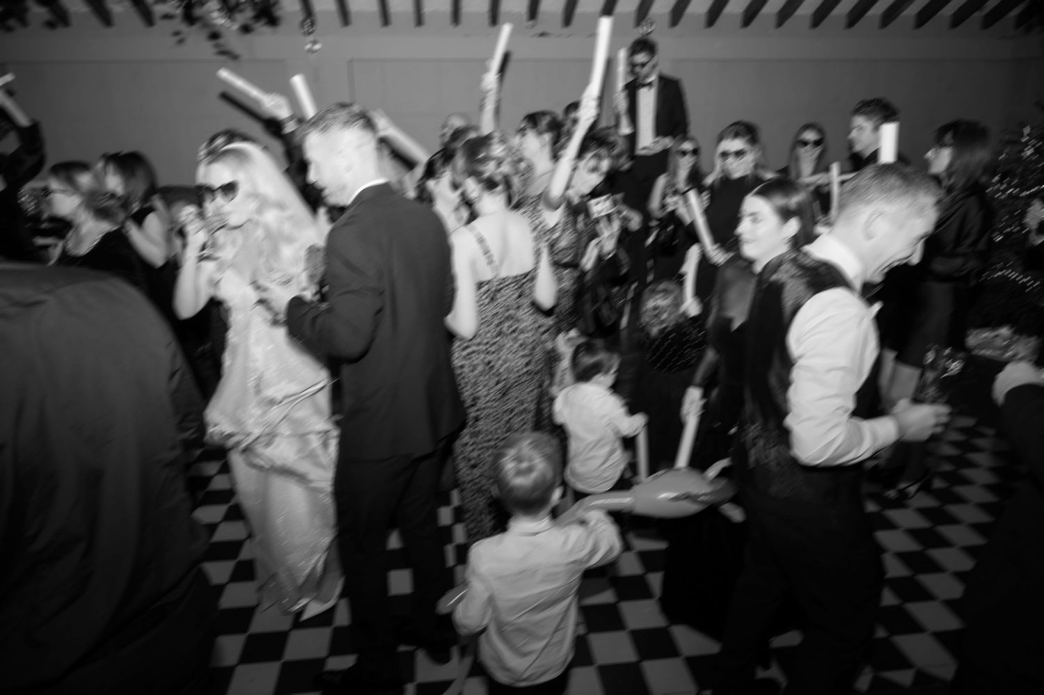 Busy dance floor filled with people in sunglasses dancing and waving glow sticks in the air.