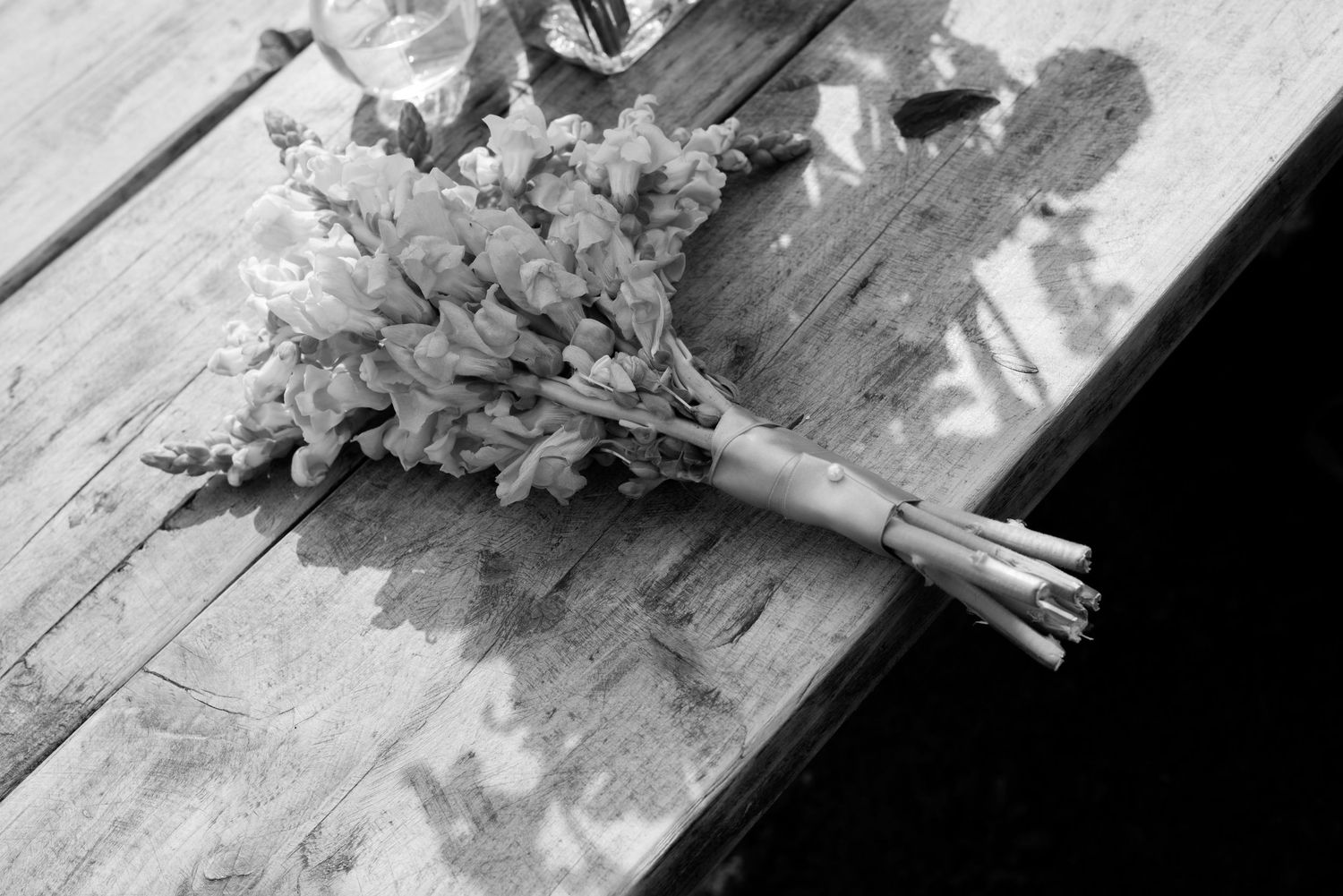 A Posey of wildflowers tied with ribbon and pearl pins lie on a wooden table in the sunshine.