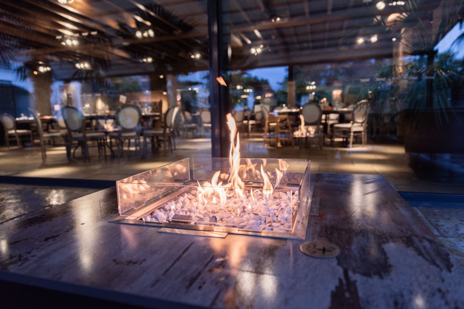 A white coal fire pit roars with orange flames at Le Petit Chateau. Behind this, an atmospheric  candlelit dining room can be seen.