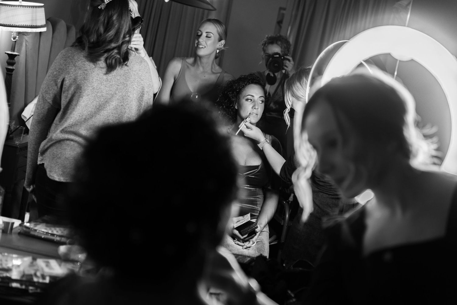 Make up artist applying product to a woman's lips using a ring light to illuminate her face in a busy make up studio.