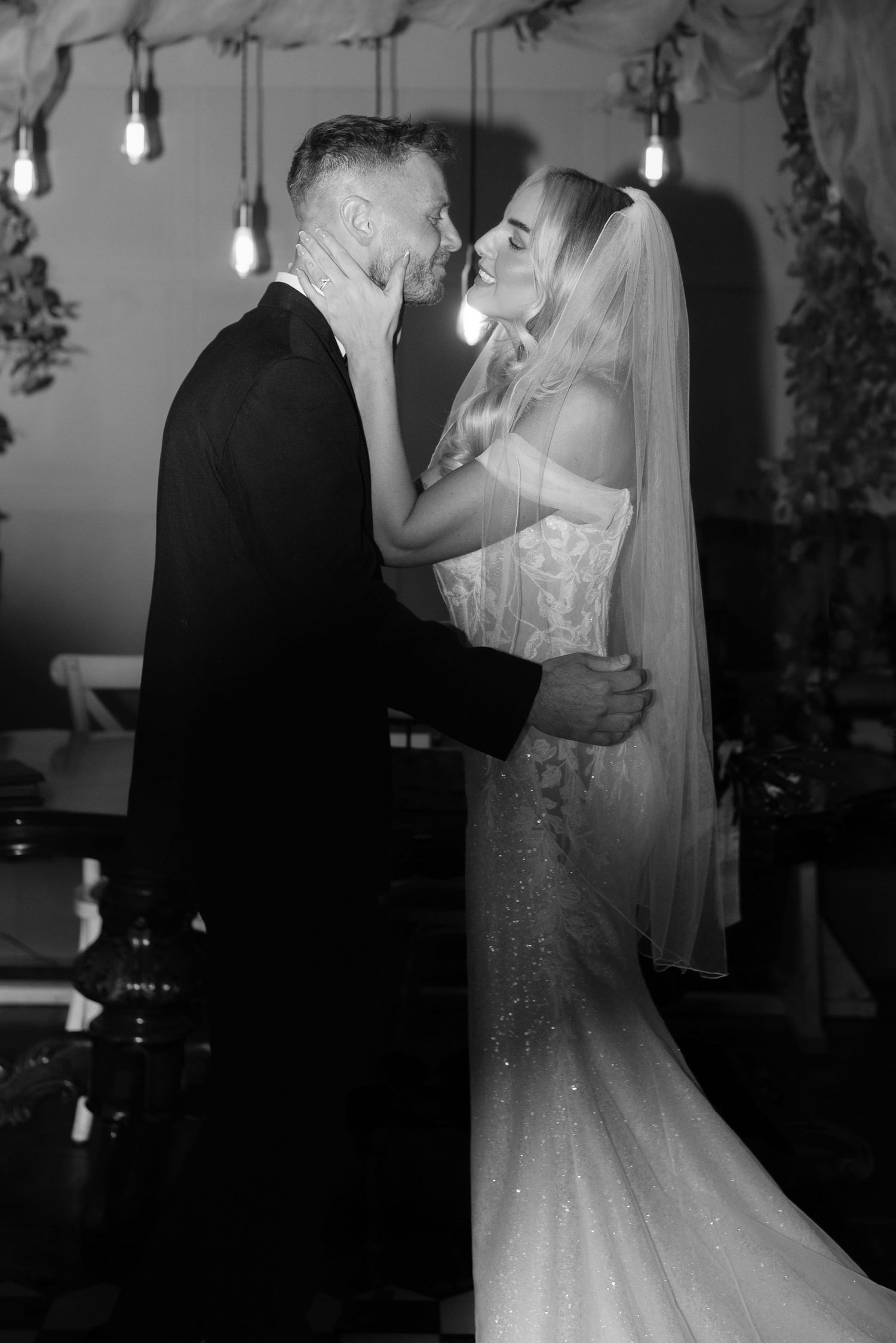 Couple sharing their first kiss in an shadowy atmospheric room surrounded by low hanging industrial style lightbulbs.
