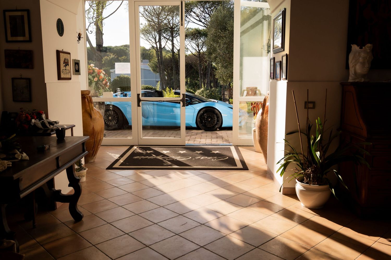 Blue Lamborghini parked outside a hotel. Bright sunshine pours through the entrance creating shadows across the car and tiled lobby floor.