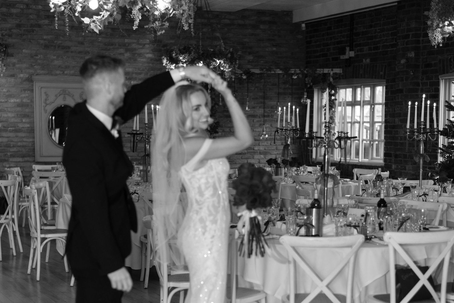 A man spinning his partner around and dancing with her in a dining room amongst tables decorated with candelabras and ribbons.