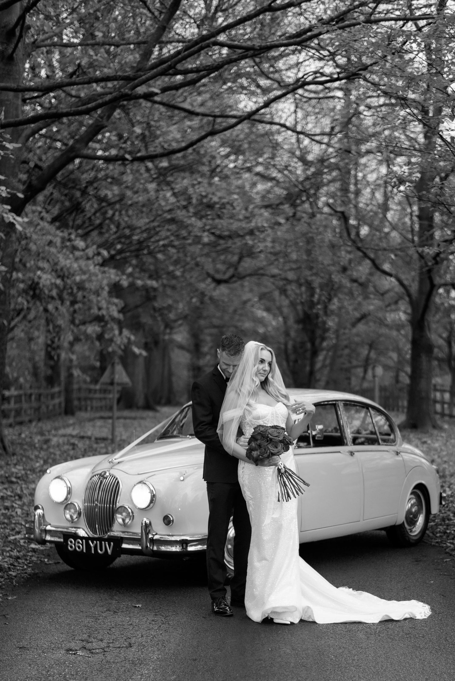 Groom holds his bride by the waist from behind, he rests his head on hers as she leans in to him and looks off into the distance.