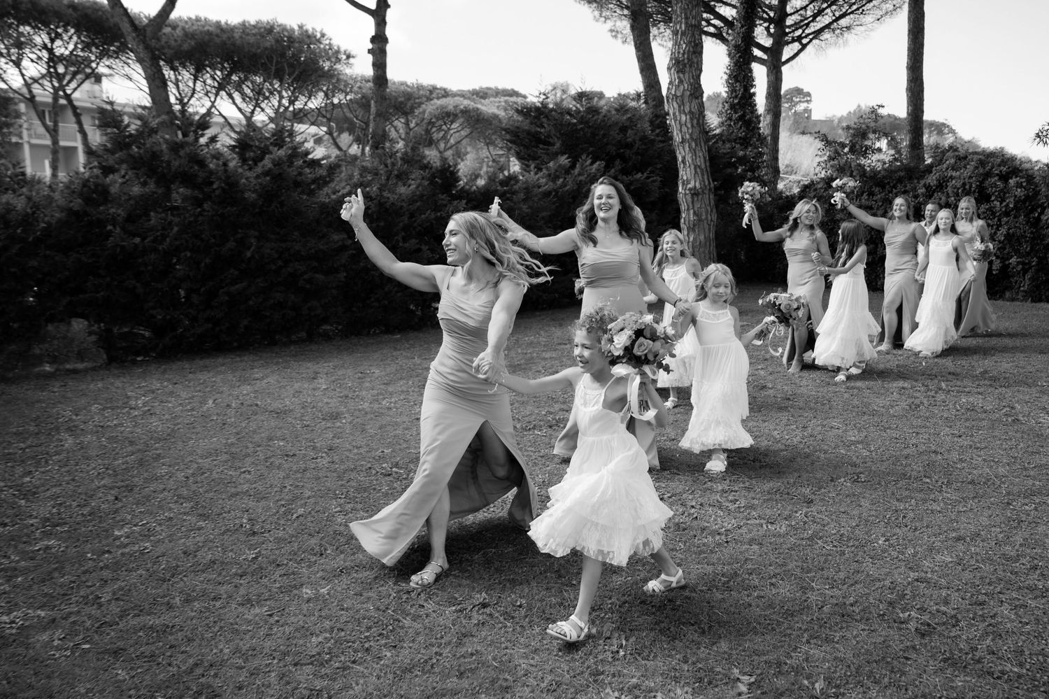 Bridesmaids walking hand in hand celebrating a wedding ceremony, smiling holding their flowers in the air in celebration.