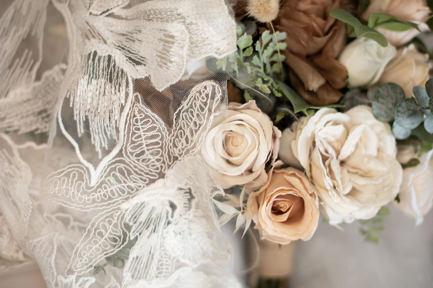 A cream, orange and brown rose bouquet  draped with an intricate lace wedding gown patterned with leaves.