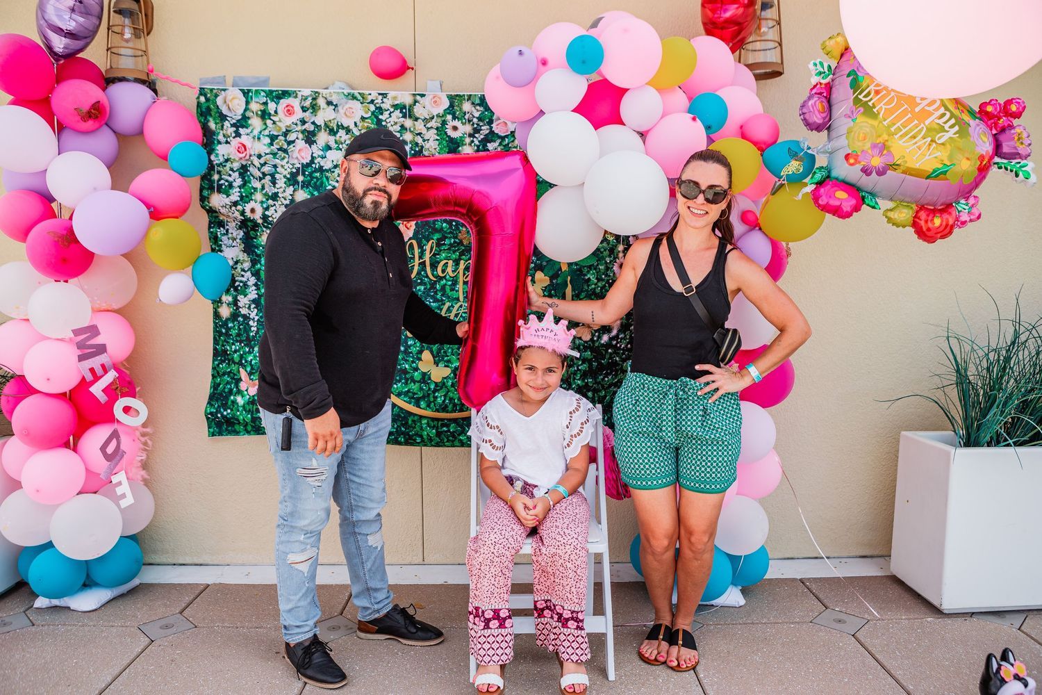 Family posing with pink number 7 balloon at colorful birthday party balloon arch.