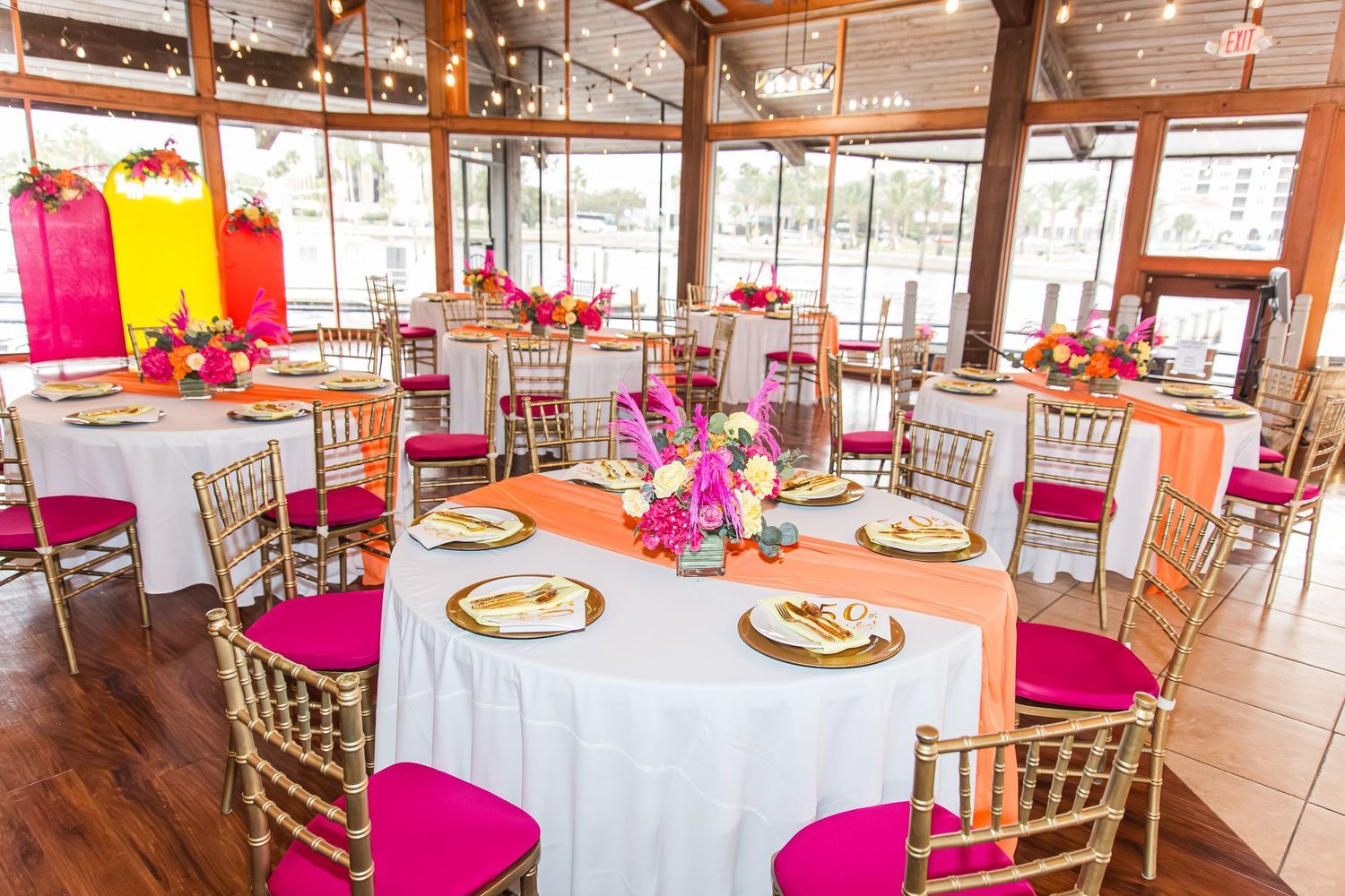 A beautifully decorated event venue with round tables, gold chiavari chairs, and pink floral centerpieces.