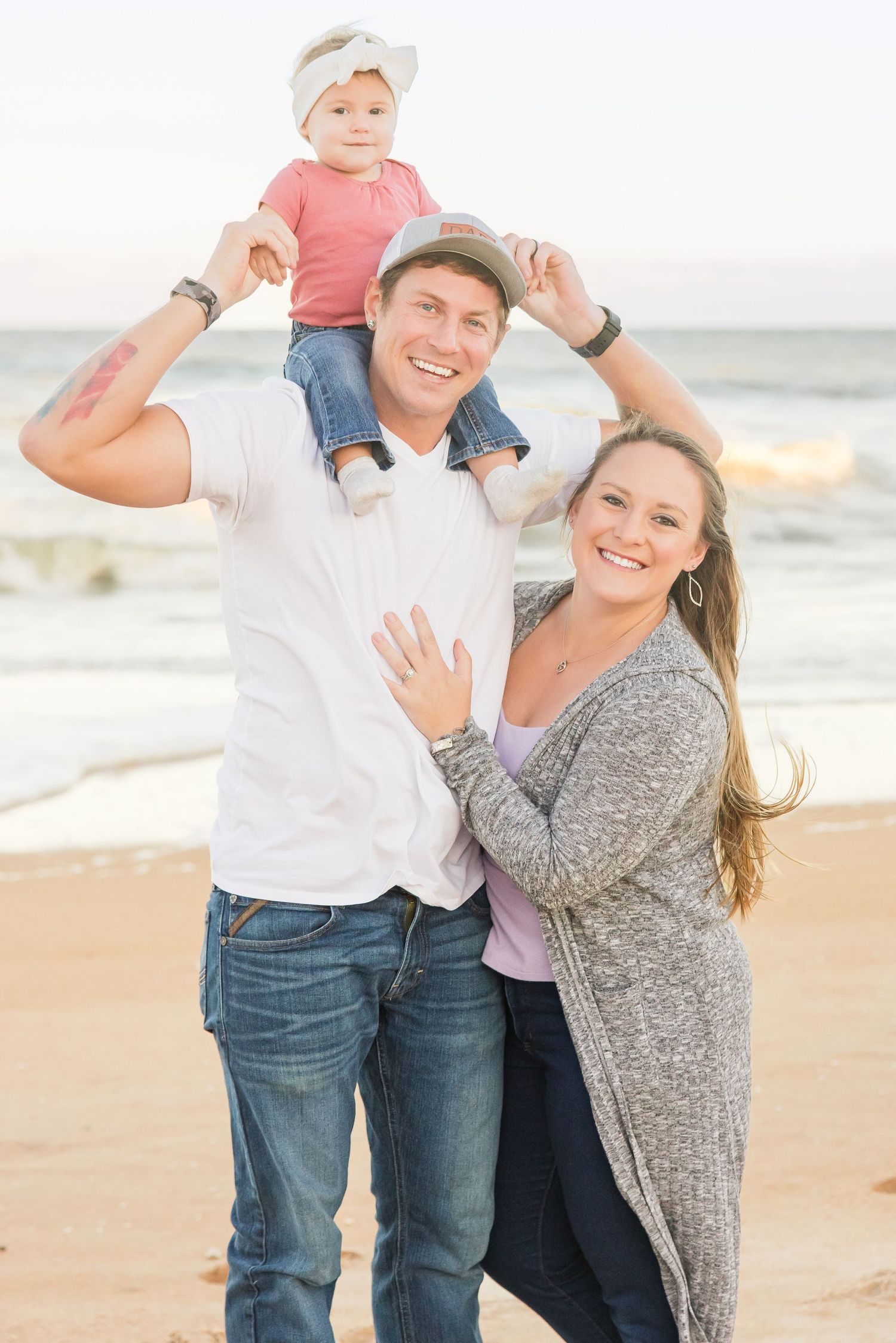 Smiling couple on beach with toddler sitting on fathers shoulders.