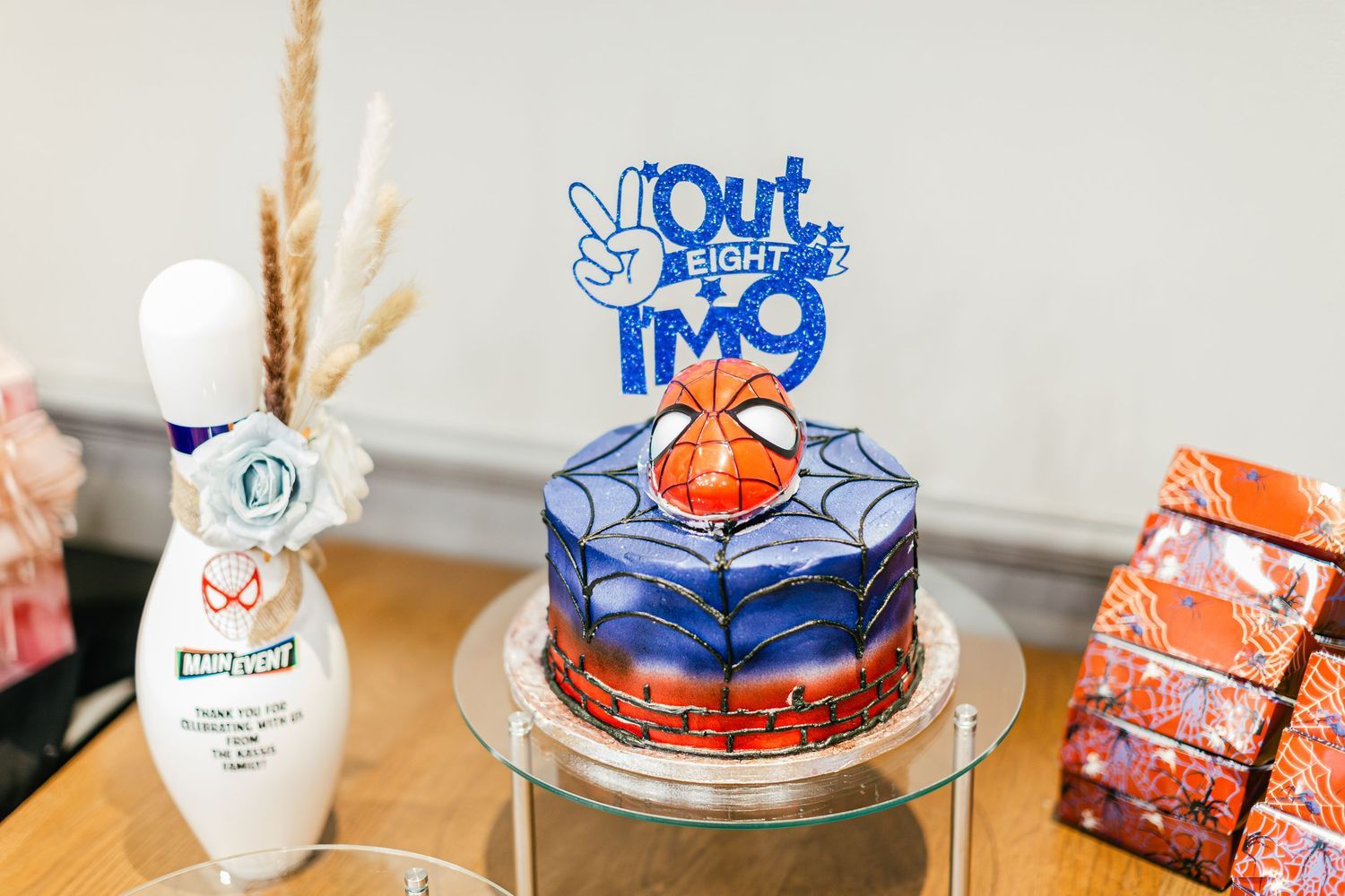 Spider-Man themed birthday cake with Out of Eight IM9 topper on a glass table.