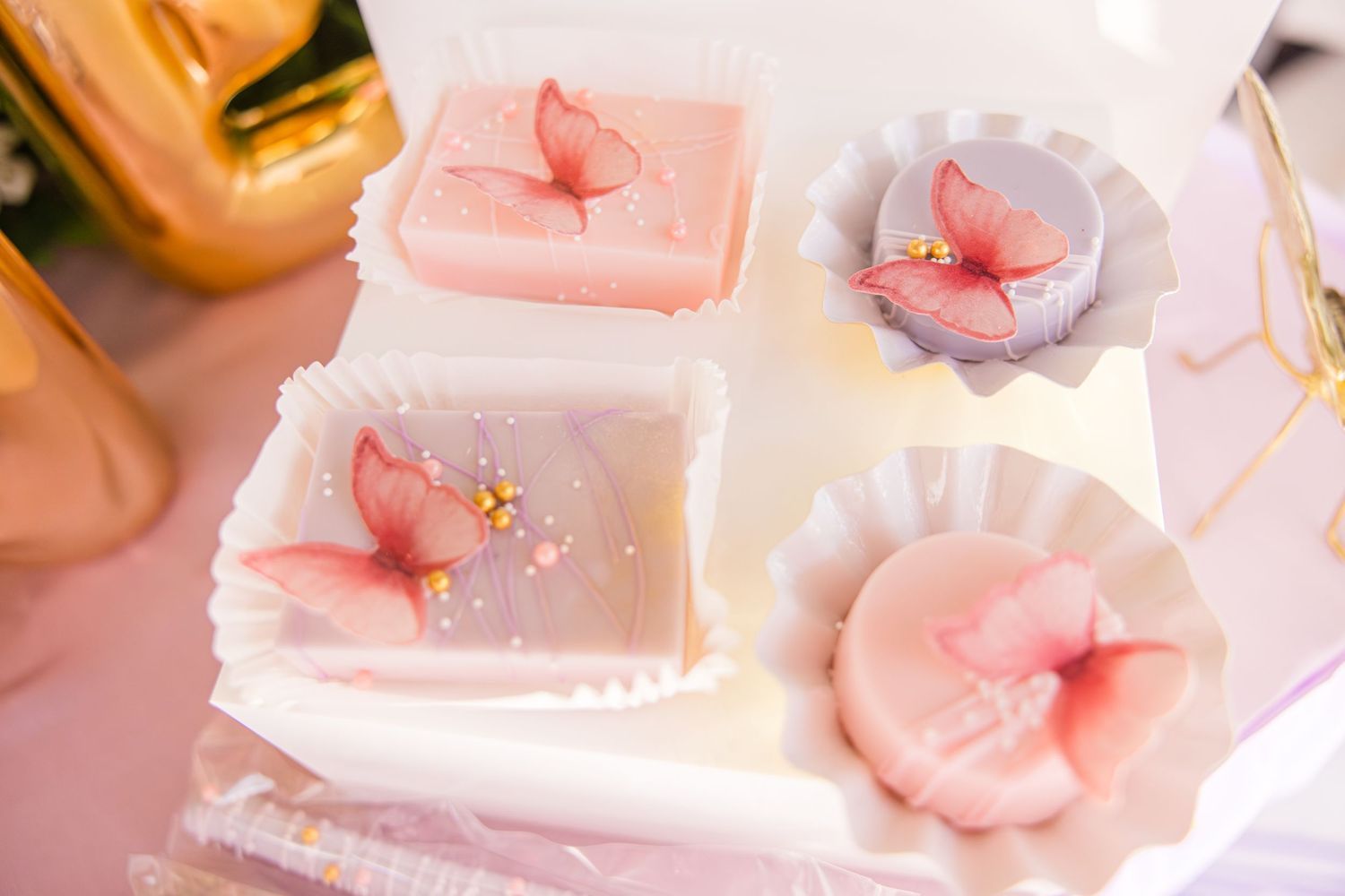 Elegant pink butterfly-decorated desserts in white paper cups for a birthday party.