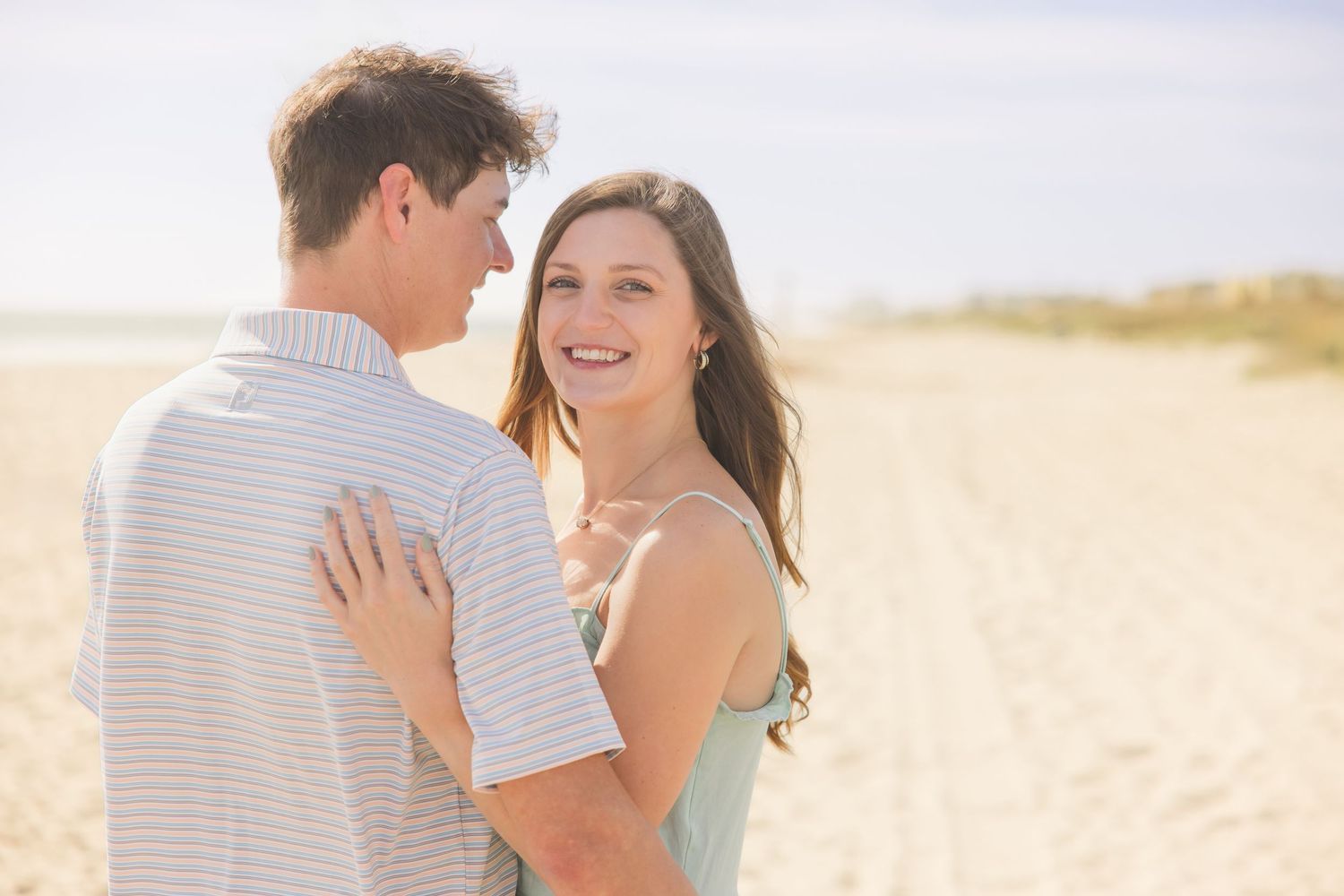 Young couple sharing a romantic moment on a sunny beach, woman smiling while embracing her partner.