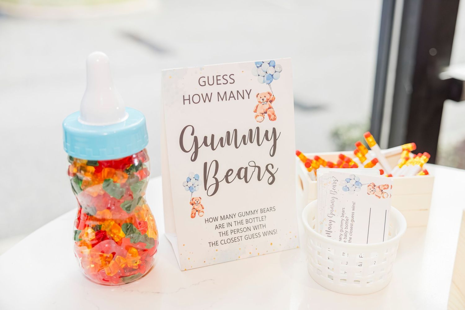A baby shower guessing game station featuring a baby bottle filled with gummy bears and a decorative sign.
