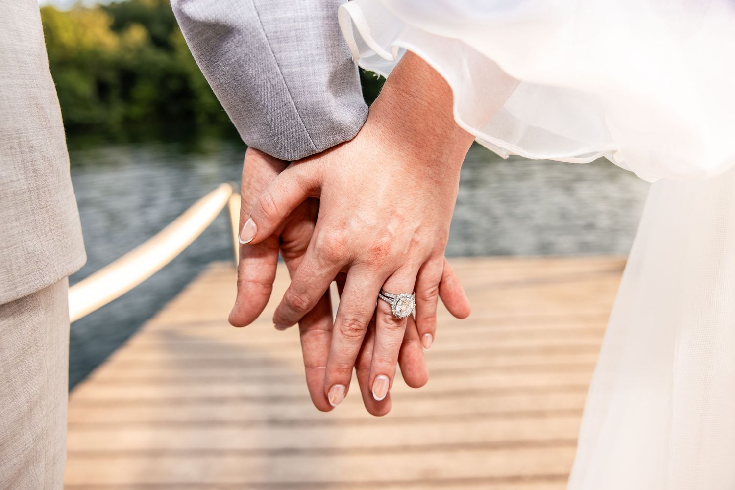 Close-up of newlyweds holding hands showing diamond engagement ring on wooden dock.