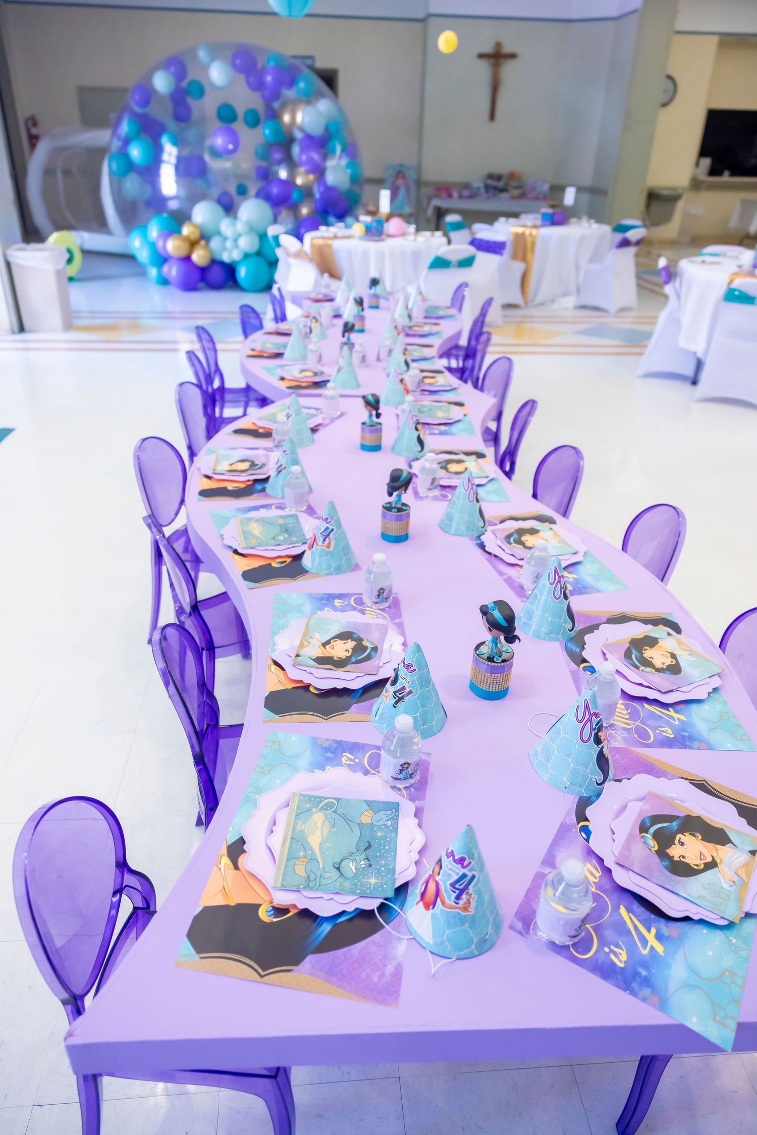 Purple Jasmine themed kids birthday party table setup with matching chairs plates and party hats.