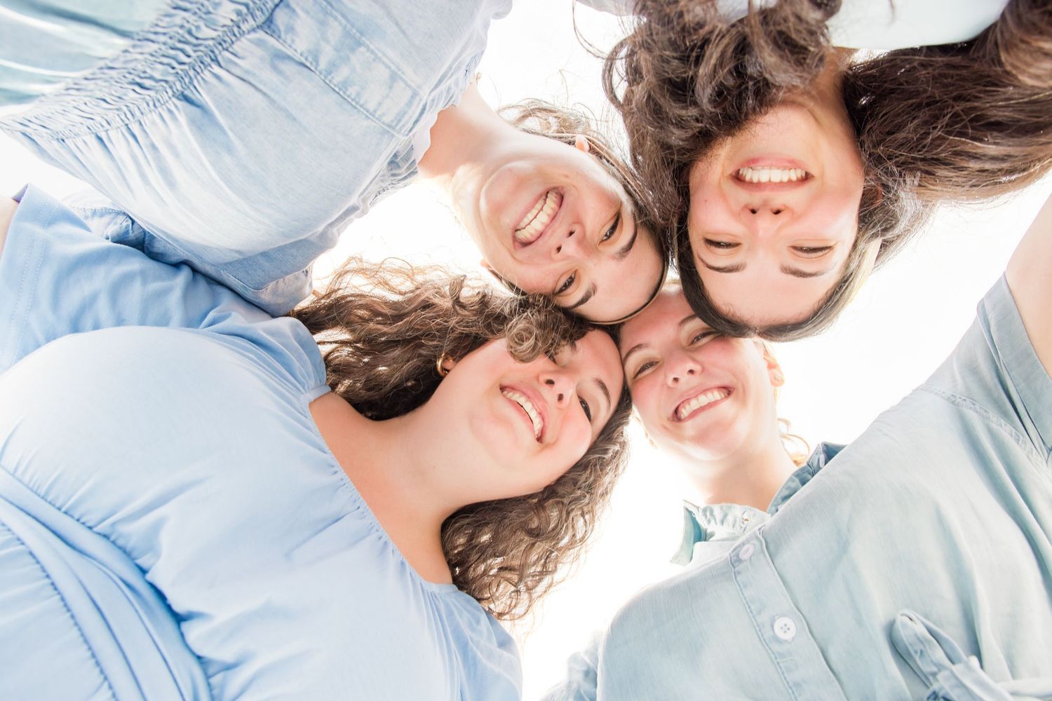 Four smiling women huddling together heads touching viewed from below.