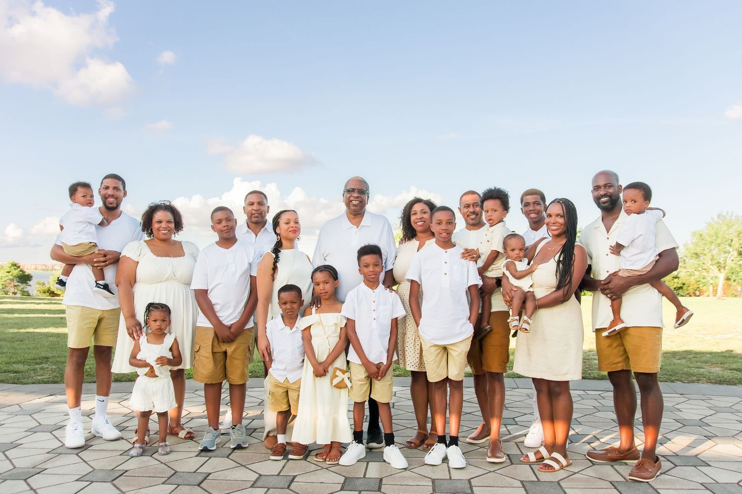 Large extended African American family posing together outdoors in coordinating white and tan outfits.