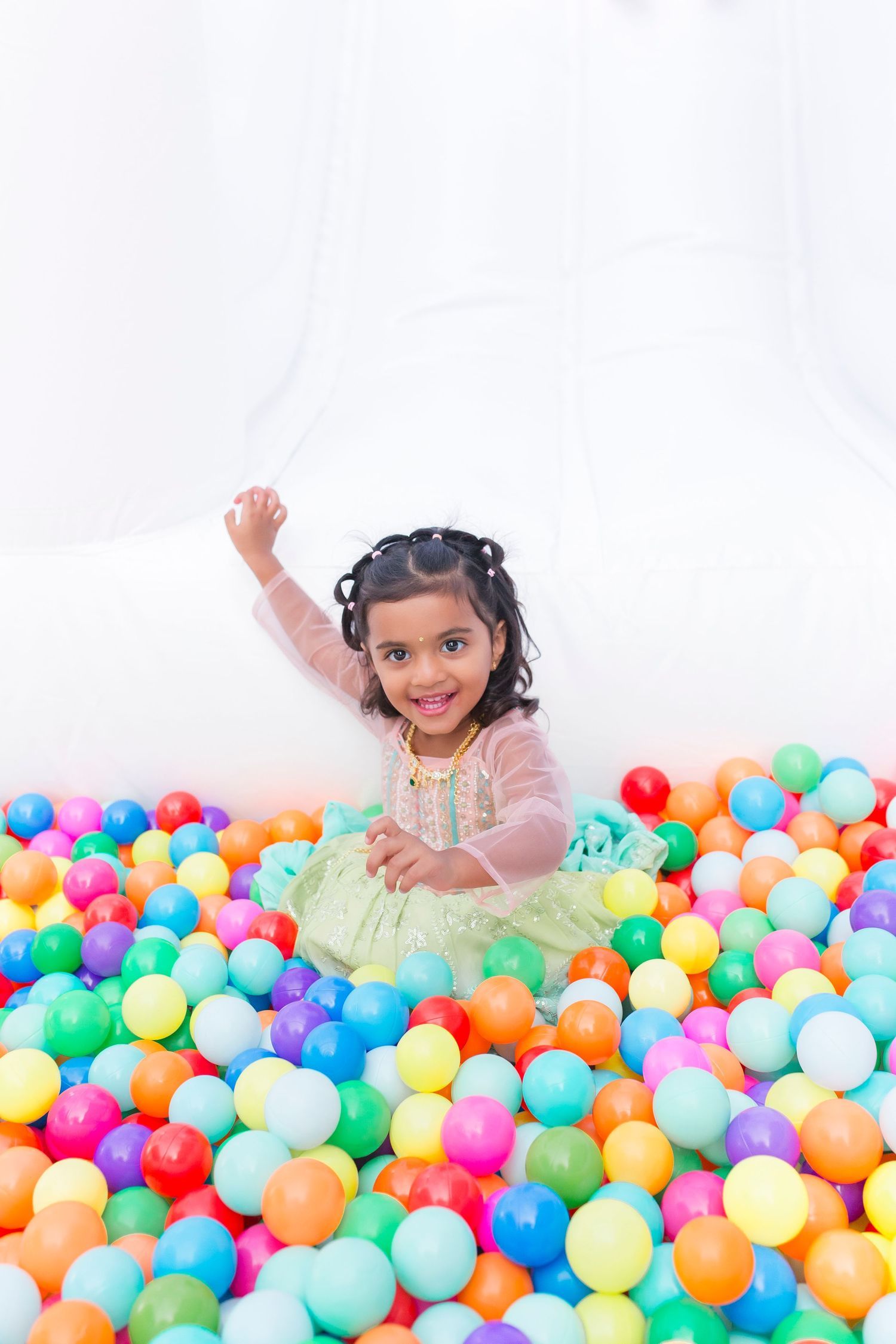 A happy young girl plays in a colorful ball pit at a birthday party celebration.