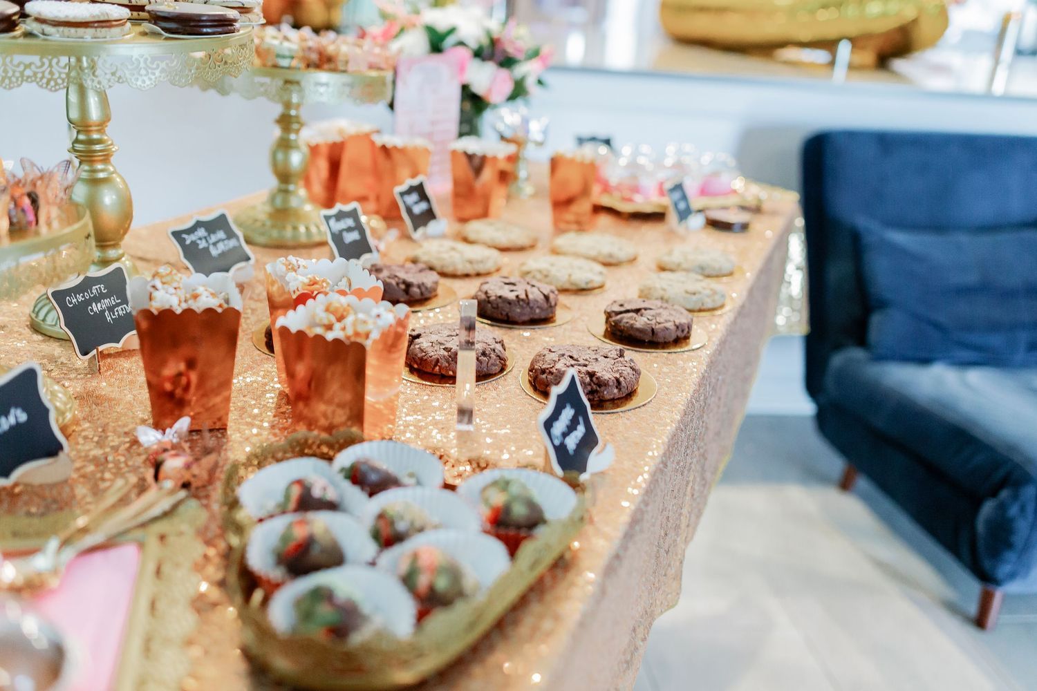 Elegant dessert table with cookies, donuts, and treats on a gold sequin tablecloth at a party.
