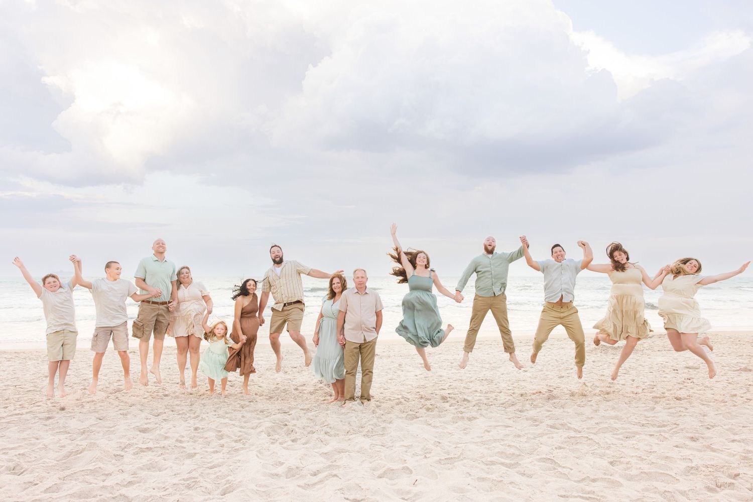 Joyful extended family jumping together on a sandy beach under a cloudy sky.