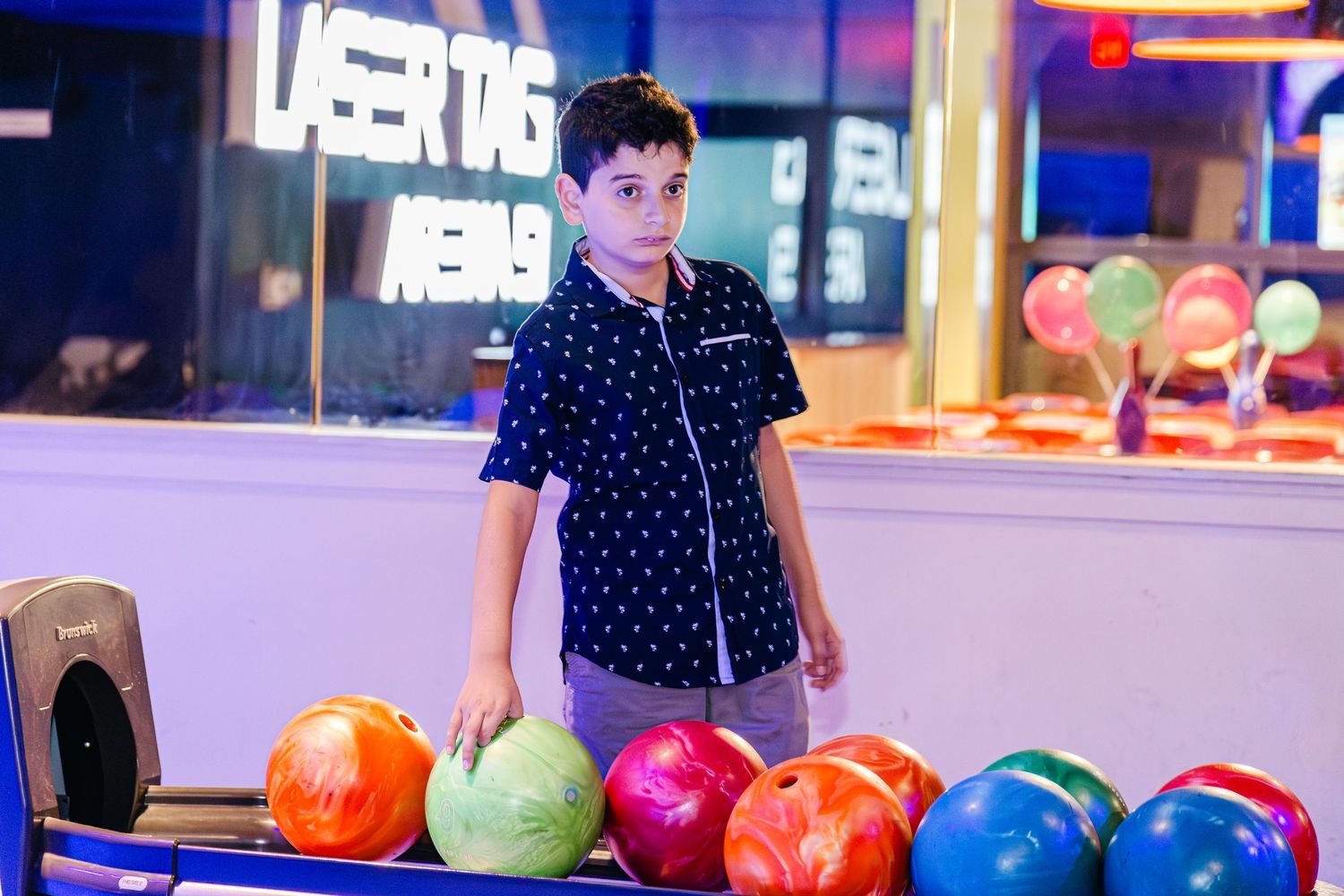 Young boy selecting a colorful bowling ball at a laser tag and bowling entertainment center.