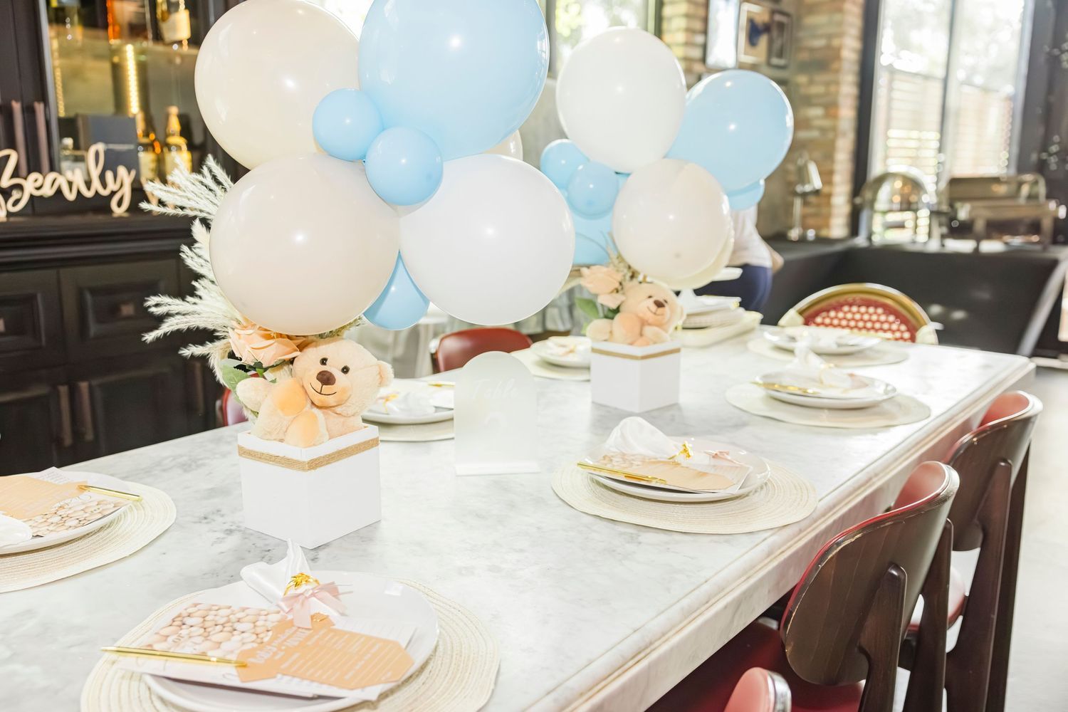 An elegantly set table with blue and white balloon centerpieces and teddy bear decorations for a baby shower.
