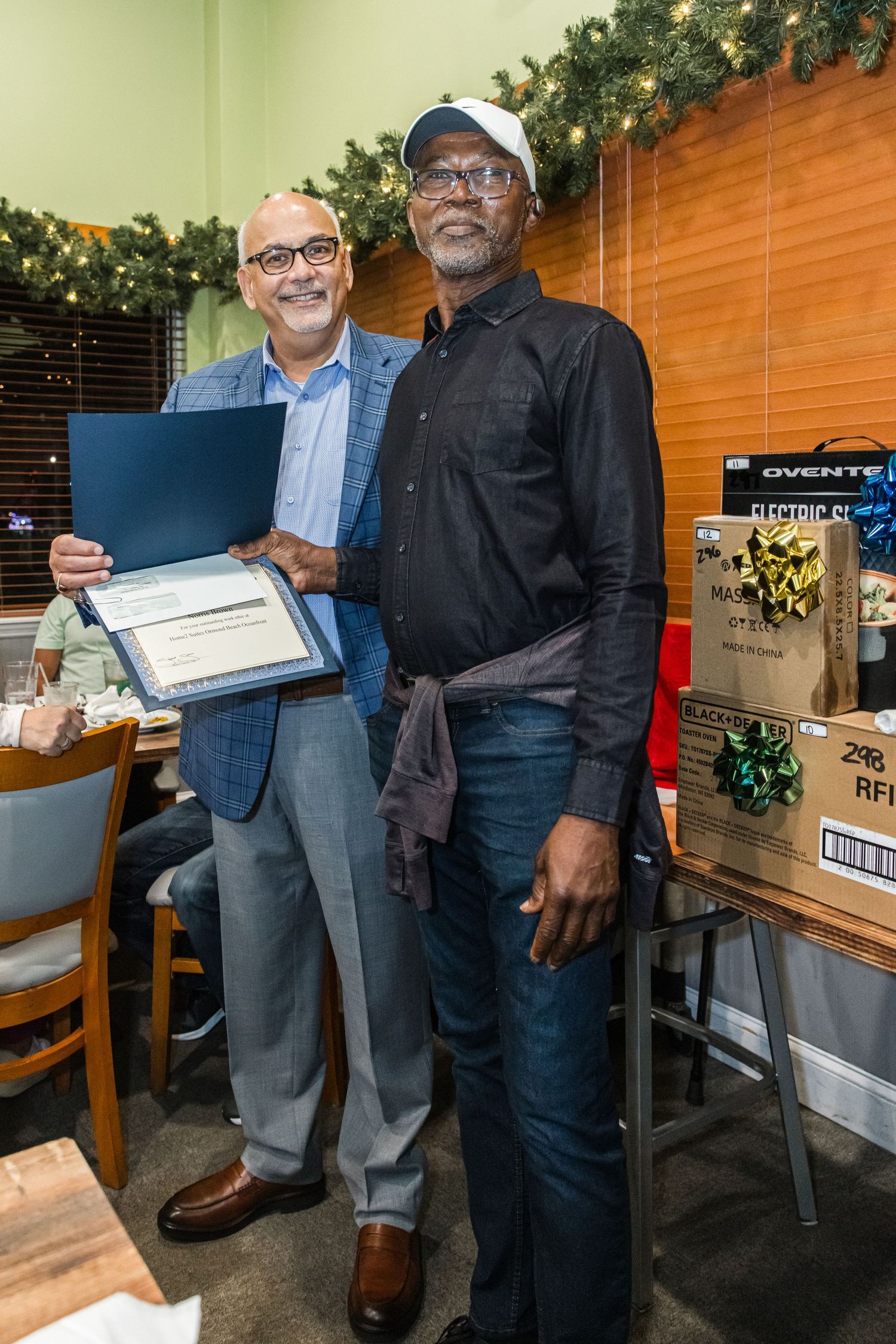 Two men pose together holding a certificate of recognition at holiday dinner event.