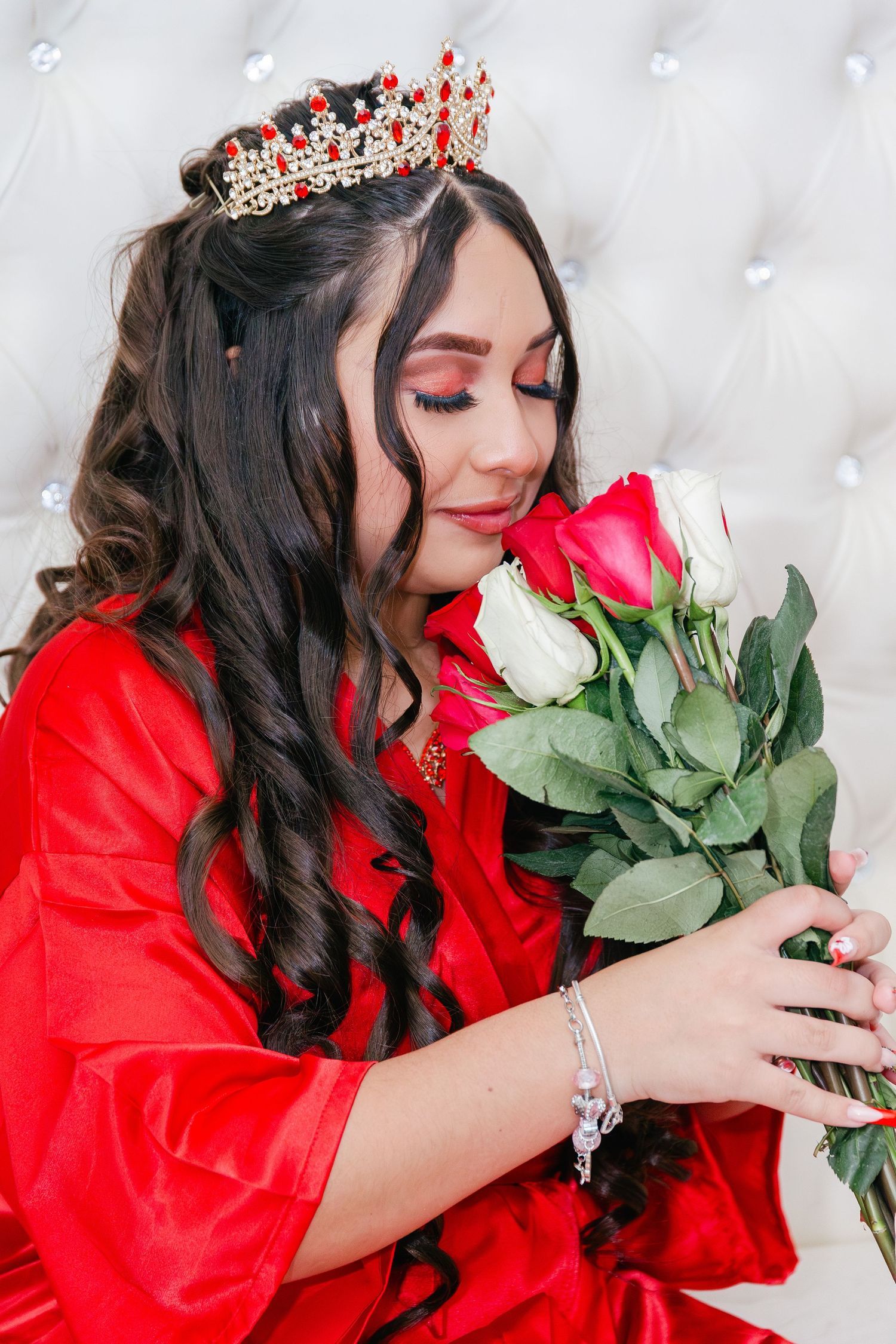 Beautiful woman in red dress wearing a crown smells a bouquet of red and white roses.