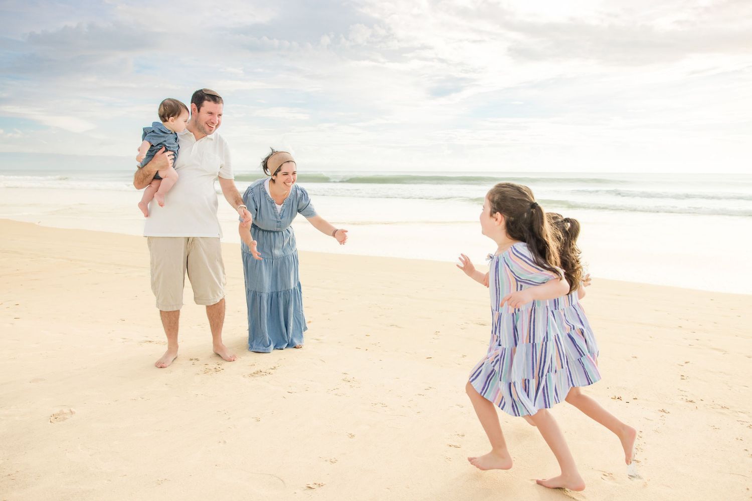 Happy family playing together on sunny white sand beach near ocean.