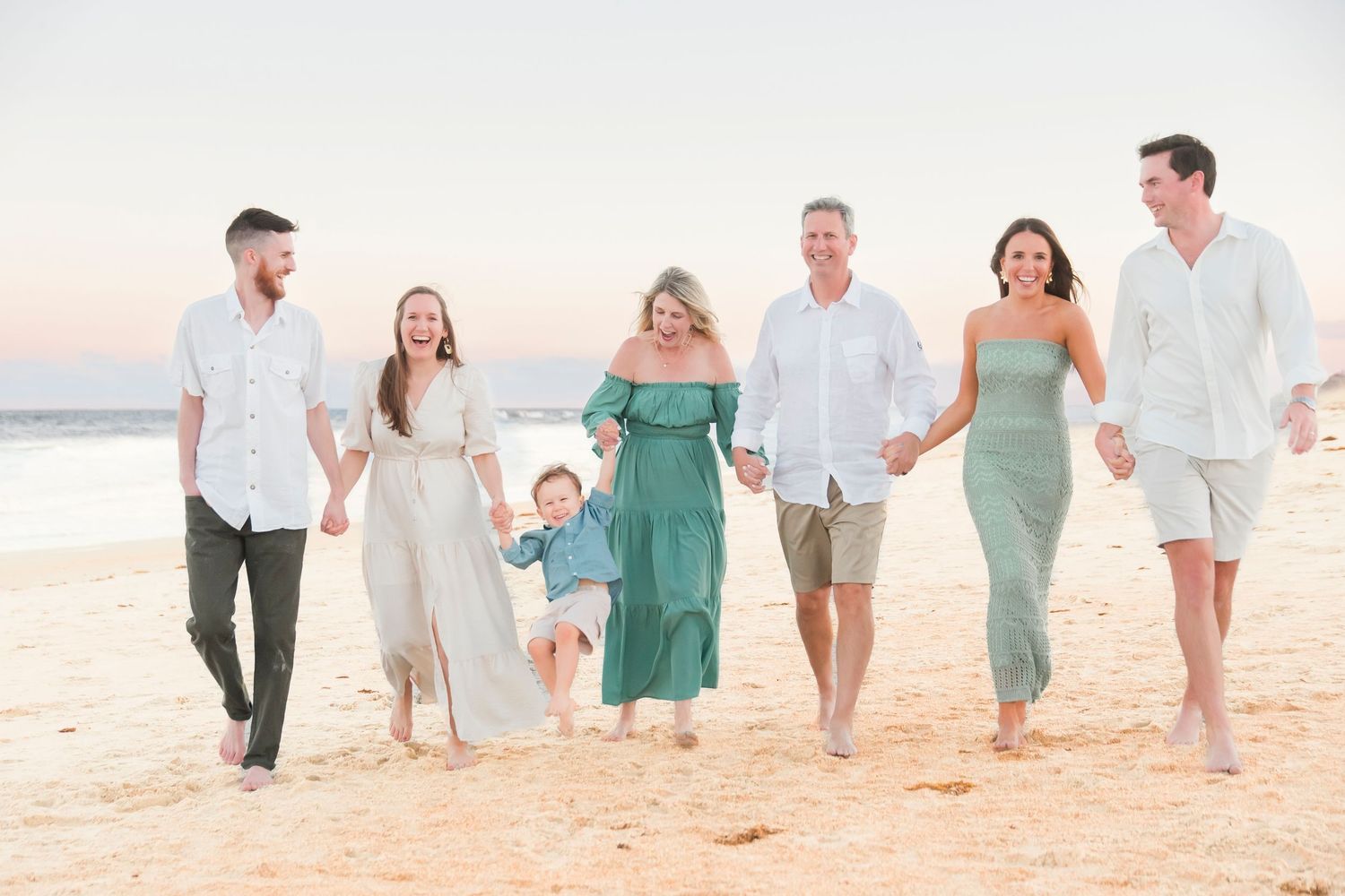 Happy multi-generational family of seven walking hand-in-hand on a beach at sunset.