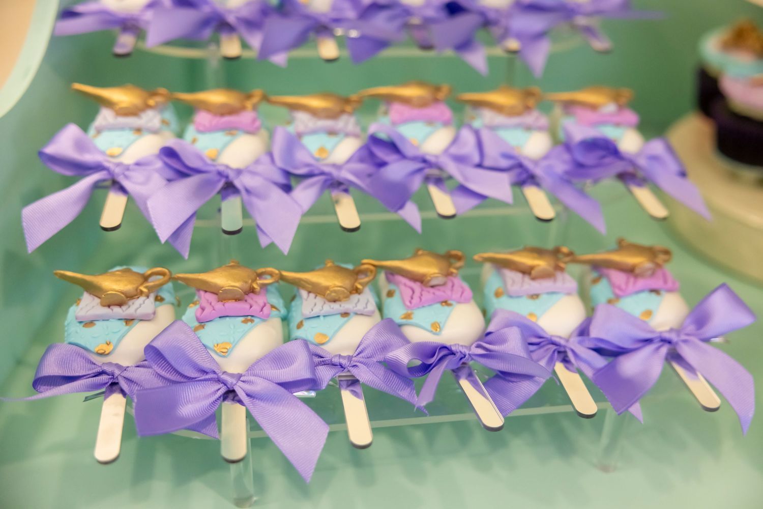 Rows of purple ribbon-tied unicorn party favors with gold accents arranged on a teal surface.