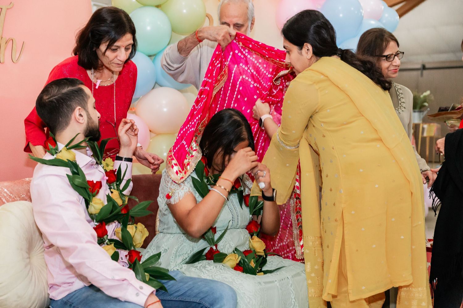 Family members placing a red dupatta over a woman during a traditional South Asian ceremony.
