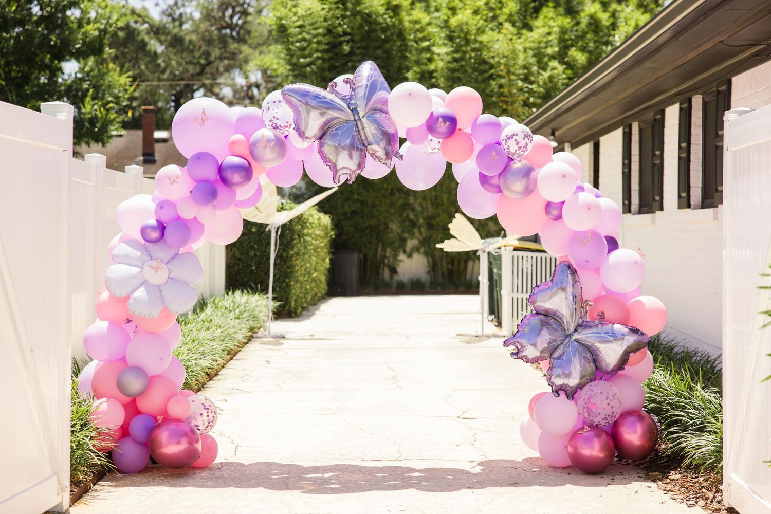Pink purple and silver balloon arch with butterfly balloons at outdoor birthday party.