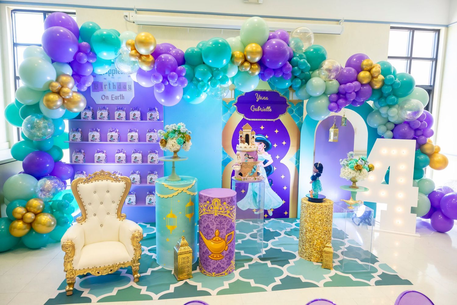 Princess Jasmine Aladdin themed birthday party backdrop with teal purple gold balloon arch and white throne chair.