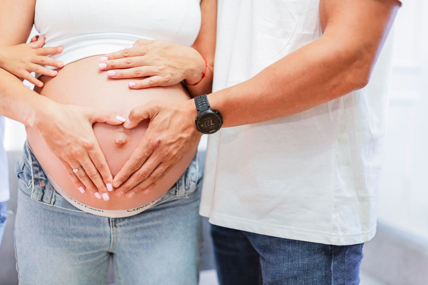 Couple forming a heart shape with their hands on a pregnant woman's baby bump.