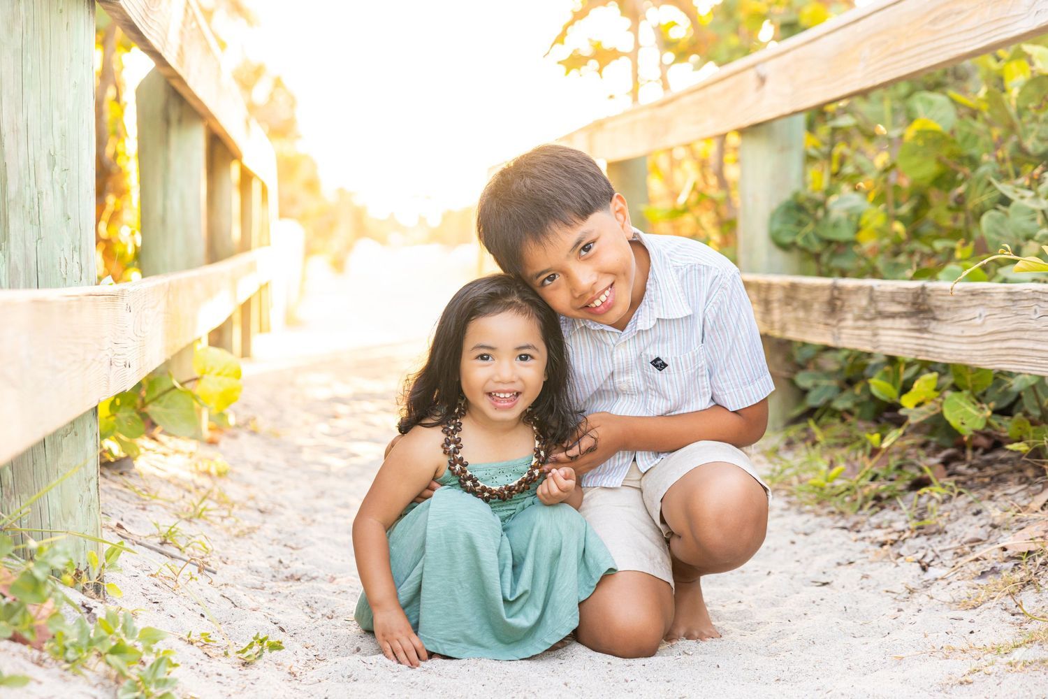Young Asian brother and sister smiling together on a sandy beach boardwalk path.