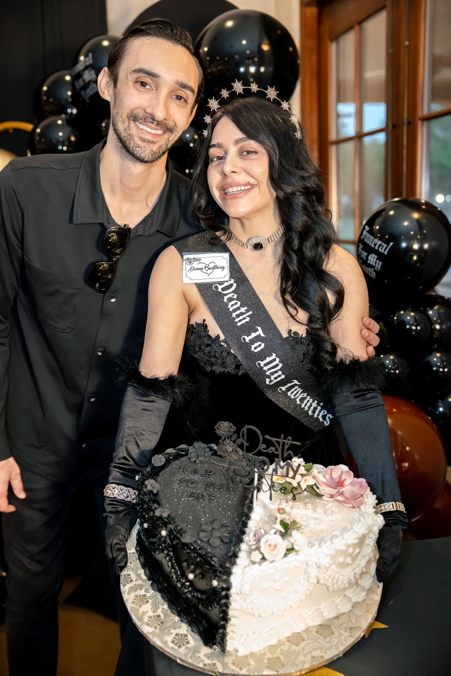 Couple smiles together holding black and white Death to My Twenties themed 30th birthday cake with balloons.