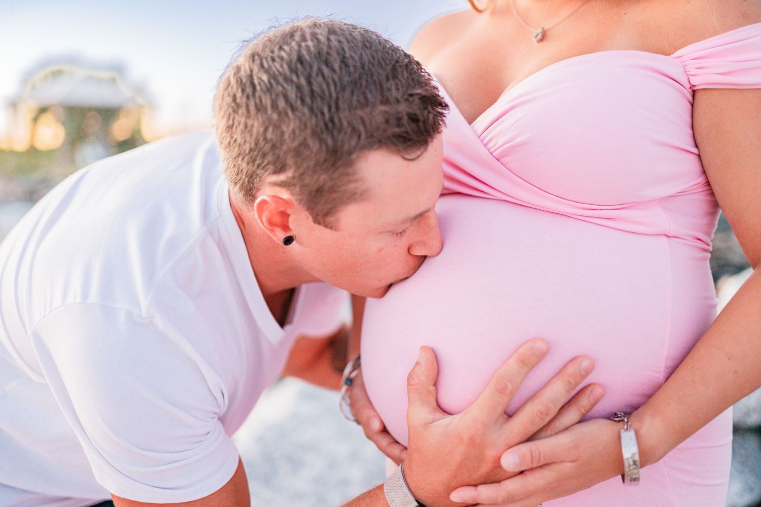 Man kissing pregnant woman's belly outdoors during a maternity photo session.