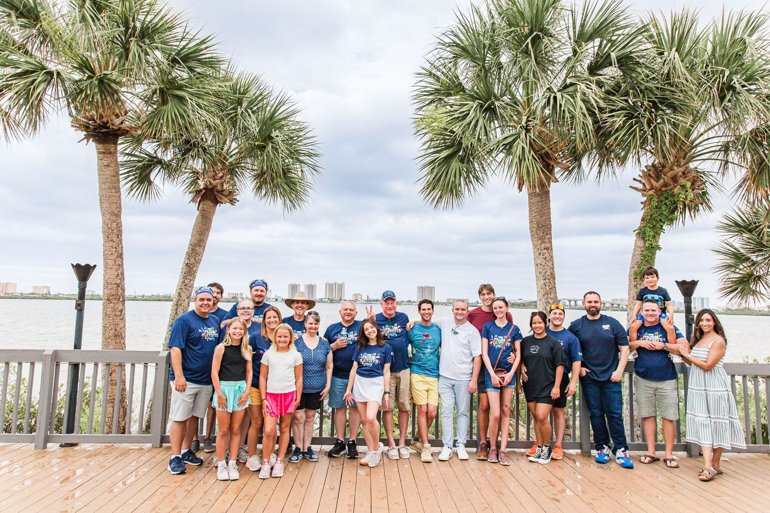 Large group of Prism Playoffs event participants pose together on a waterfront deck near palm trees.