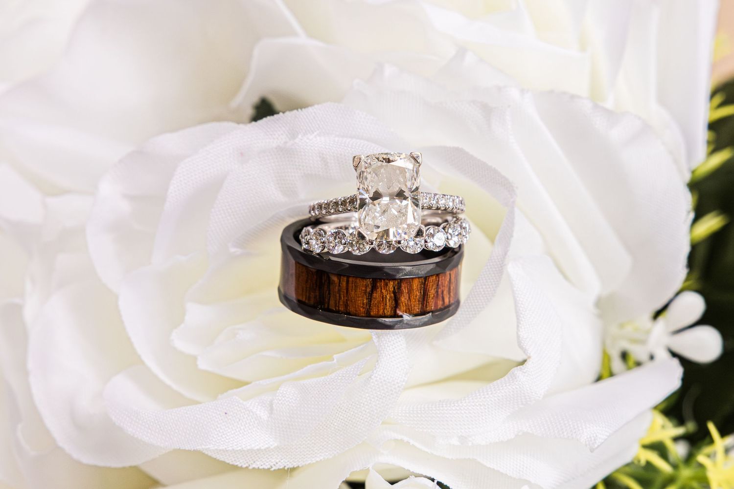 Wedding rings displayed on white rose petals, featuring diamond ring and wood grain band.